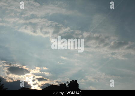 Les rayons du soleil venant par de sombres nuages sur ciel bleu Banque D'Images