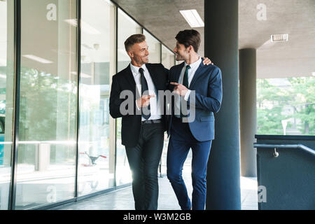 Portrait of two smiling businessmen partenaires habillé de la fonction de montrer du doigt tout en marchant à l'extérieur du centre d'emploi pendant les mee Banque D'Images