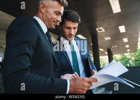 Image de jeunes hommes d'affaires partenaires habillé de la fonction de l'extérieur office center et la tenue des graphiques au cours de réunion de travail papier Banque D'Images
