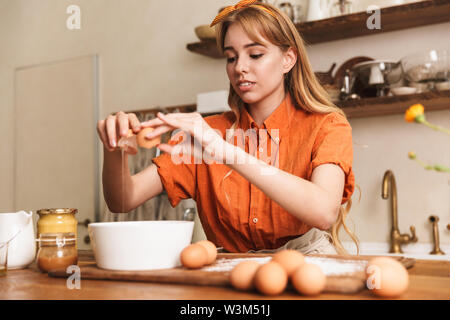 Photo d'une jeune fille blonde chef de cuisine dans la cuisine avec des oeufs. Banque D'Images