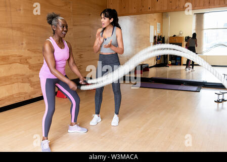 Entraîneur personnel encourageant mature woman exercising with ropes in gym Banque D'Images