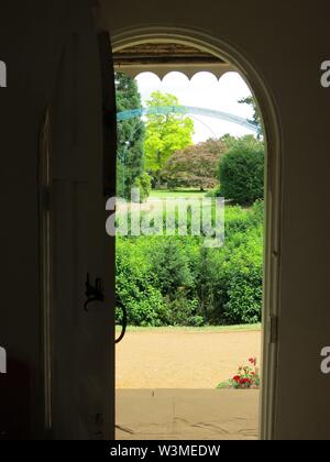 Une porte en bois donne un aperçu de l'extérieur jardin ensoleillé, avec un treillis bleu en arrière-plan Banque D'Images