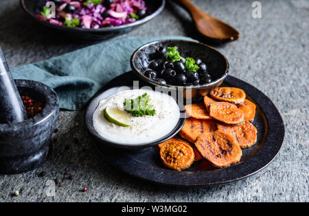 Tranches de pommes de terre frits servis avec trempette de crème sure, olives noires et salade faite de chou rouge, oignon rouge et betterave Banque D'Images