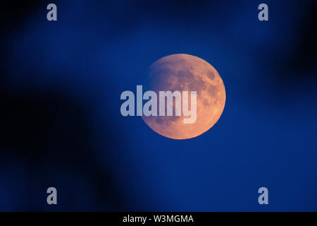 Schwerin, Allemagne. 16 juillet, 2019. La pleine lune s'allume en rouge au début de l'entrée partielle dans l'ombre de la terre. Les badauds peuvent observer une éclipse lunaire partielle sur l'Allemagne. Entre 22h le mardi et 13h le mercredi des parties de la terre se trouvent dans le noyau de la ombre de la terre et la lune brillent dans le ciel rouge rouille. Credit : Jens Buettner/dpa-Zentralbild/dpa/Alamy Live News Banque D'Images