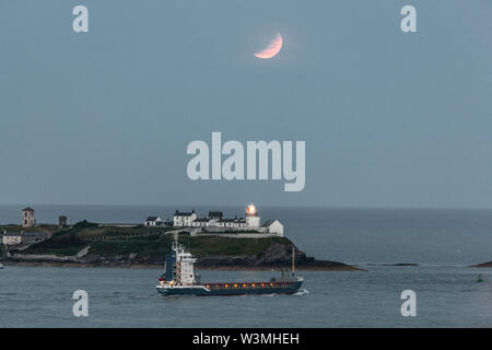 Athelstan, Cork, Irlande. 16 juillet, 2019. L'esprit celtique cargo quitte le port en tant qu'éclipse partielle de la lune se produit dans la Roches Point Lighthouse dans Port de Cork, Irlande. Crédit : David Creedon/Alamy Live News Banque D'Images