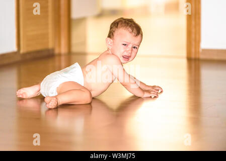 Bébé sur le plancher de sa chambre en couches, avec un visage en colère et pleurer tout en rampant. Banque D'Images