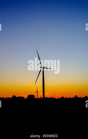 Silhouette noire des éoliennes contre ciel bleu et orange au crépuscule. Banque D'Images