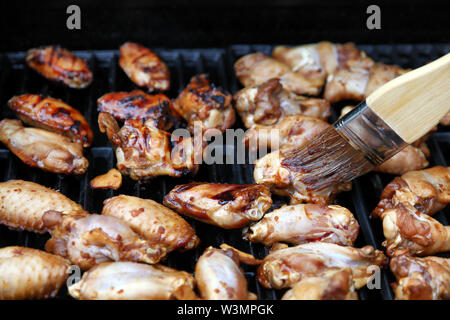 Close up of an open barbecue la cuisson des ailes de poulet, tout en étant brossé avec sauce épicée Banque D'Images
