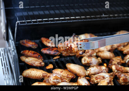Close up of an open barbecue la cuisson des ailes de poulet avec tong holding d'une seule pièce Banque D'Images