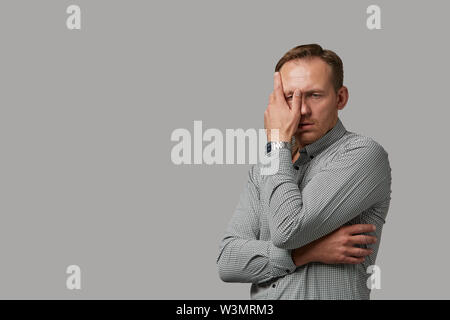 Un homme en habits cache son visage avec ses mains sur un fond gris. Émotif, brave face. Isolé sur fond blanc Copy space Banque D'Images