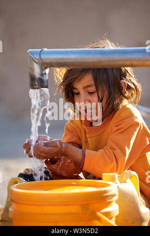 Un enfant afghan recueille l'eau d'une pompe à main à Maslakh camp pour personnes déplacées, à la périphérie d'Herat. Il n'est plus un camp officiel, mais encore beaucoup de gens de différentes provinces reculées continuent à venir de se mettre à l'abri de difficultés dans les zones rurales. L'Afghanistan. 20 juin 2007. Banque D'Images