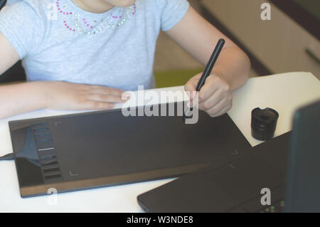 Fille enfant s'appuie sur une tablette graphique en étant assis à une table avec un ordinateur portable Banque D'Images