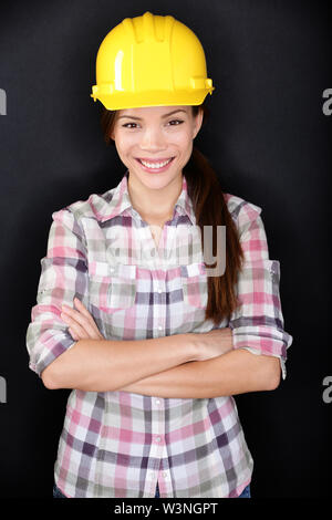 Female construction worker, propriétaire de maison en rénovation ou ingénieur posant sur fond noir. Jeune femme portant un casque de protection jaune souriant heureux. Société multiraciale modèle asiatique. Banque D'Images