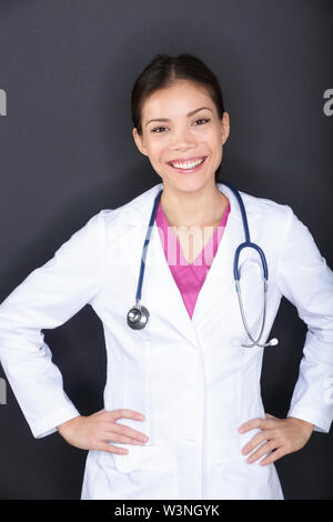 Femme médecin woman portrait. Happy smiling young medical professional in lab coat with stethoscope looking at camera sur fond noir. Caucase Asie multi-ethnique modèle féminin. Banque D'Images