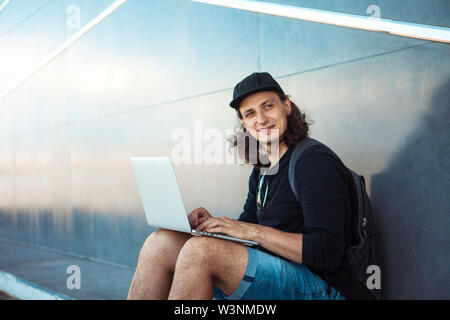 Un jeune homme, assis sur une planche à roulettes jaune, essaie de synchroniser un ordinateur portable avec un téléphone. Apparemment, il s'est passé. Heureusement qu'il se pencher sur le châssis. Banque D'Images