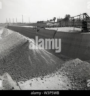 Années 1950, photo historique montrant une grande carrière de sable ou gravier avec grue d'où la matière première pour produire des briques est tiré, avec les cheminées de l'usine de fabrication des briques dans la distance, England, UK. Banque D'Images