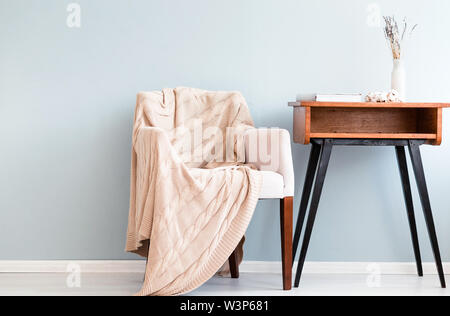 Photo de fauteuil avec support de table et rétro plaid contre un mur bleu Banque D'Images