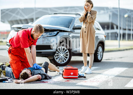 Ambluence application travailleur de soins d'urgence aux blessés l'homme purge allongé sur le passage piétons, désespoir femme debout sur l'arrière-plan Banque D'Images