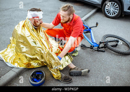 Ambluence couverture travailleur homme blessé avec une couverture thermique, fournissant des soins d'urgence après l'accident de la route Banque D'Images