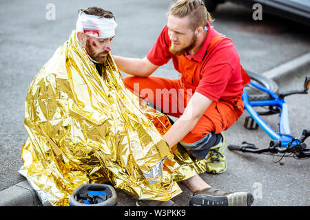 Ambluence couverture travailleur homme blessé avec une couverture thermique, fournissant des soins d'urgence après l'accident de la route Banque D'Images