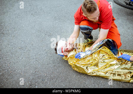 Ambluence couverture travailleur homme blessé avec une couverture thermique, fournissant des soins d'urgence après l'accident de la route Banque D'Images