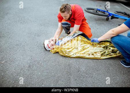 Ambluence couverture travailleur homme blessé avec une couverture thermique, fournissant des soins d'urgence après l'accident de la route Banque D'Images