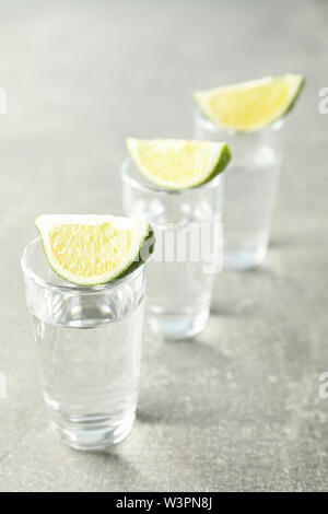 Tequila shots avec des tranches de citron vert sur fond gris Banque D'Images