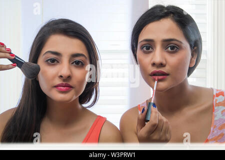 Portrait de deux adolescentes faire un miroir à la recherche dans le miroir l'application de peinture et pinceau à lèvres Banque D'Images