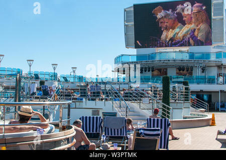 Océan Atlantique - déc 2017 : Les passagers du bateau de croisière vous détendre au bord de la piscine sur le pont supérieur en face de l'immense écran de la cinéma en plein air. Banque D'Images