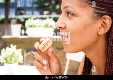 Mixed Race girl eating beau macaron au chocolat café en plein air en été. Banque D'Images