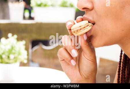 Mixed Race girl eating beau macaron au chocolat café en plein air en été. Banque D'Images