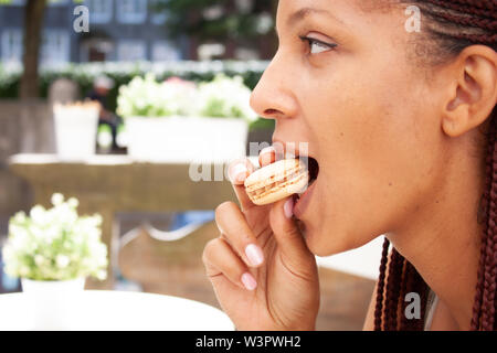 Mixed Race girl eating beau macaron au chocolat café en plein air en été. Banque D'Images