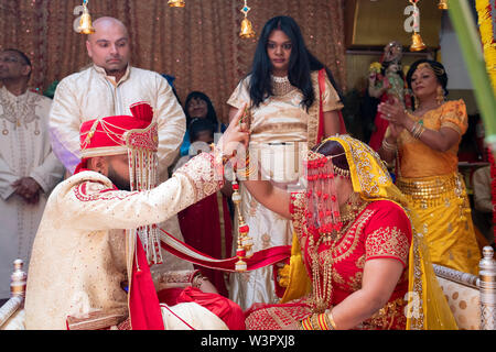 Avec leurs clients à la recherche sur, une jeune mariée et se toilettent touch mains au cours d'une cérémonie de mariage traditionnelle hindoue dans un temple à Ozone Park, Queens, New York City Banque D'Images
