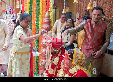 Lors d'une cérémonie de mariage traditionnelle hindoue, la grand-mère de la mariée & oncle parsemer des fleurs sur le couple. Dans un temple à Ozone Park, Queens, New York. Banque D'Images