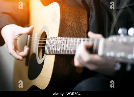 Le guitariste de noir, éclairé par la lumière orange vif, joue une belle mélodie sur une guitare à six cordes acoustique Banque D'Images