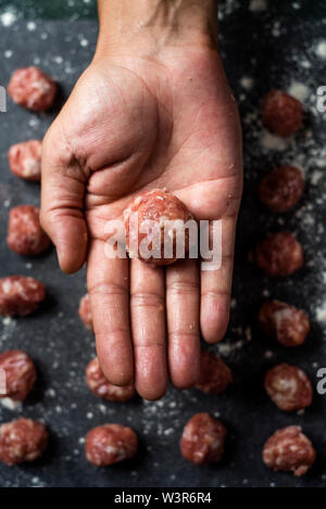 Portrait d'un homme de race blanche avec une matière meatball dans sa main, et certaines autres matières premières boulettes sur une table en bois gris foncé ou un comptoir Banque D'Images