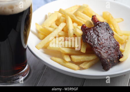 Côtes de porc grillées avec des frites et un verre de bière brune Banque D'Images