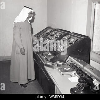 Années 1960, historique, un Arabe technicien studio portant un traditionnel à la cheville d'un garnent Thawb ou Thobe et coiffure, un keffieh, travaillant à un magnétophone dans une émission de télévision, l'Arabie Saoudite. Banque D'Images