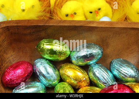 Oeufs de Pâques en chocolat coloré bol en bois et poussins jaune en arrière-plan Banque D'Images
