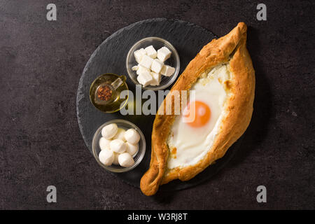 Khachapuri géorgien adjare traditionnel avec du fromage et des oeufs sur fond noir. Vue d'en haut. Banque D'Images