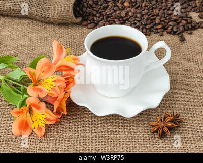 Fleur de lys péruviens d'Orange, un café chaud dans la tasse avec soucoupe élégant blanc et la dispersion des grains de café sur fond d'un sac rustique. Banque D'Images