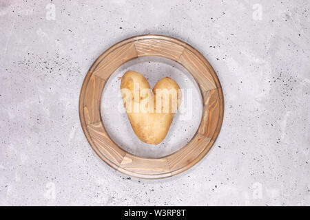 Un laid à l'intérieur de la pomme de terre en forme de coeur cadre woodem ronde au centre du fond de béton gris. Banque D'Images