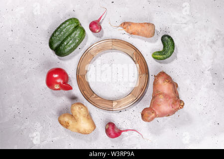 Ensemble de légumes mûrs laid posées autour du cadre en bois arrondies sur fond de béton gris. Banque D'Images