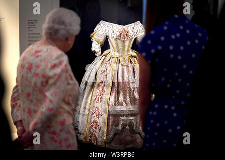 La reine Elizabeth II se penche sur le costume de la Reine Victoria pour le Stuart Ball en 1851 en tant qu'elle considère l'exposition pour marquer le 200e anniversaire de la naissance de la Reine Victoria pour l'ouverture estivale du Buckingham Palace, Londres. Banque D'Images