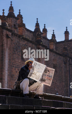 Man reading newspaper assis sur les marches de la cathédrale de la Plaza de Armas, la place principale, rétroéclairé à Cusco, Pérou, Amérique du Sud Banque D'Images