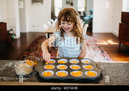 Jeune fille assise dans la cuisine avec remplissage muffins Pêches fraîches Banque D'Images