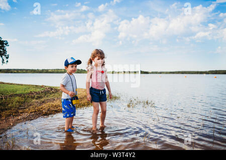 Jeune garçon et fille debout dans l'eau au lac portant des jumelles