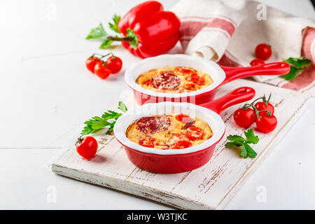 Frittata aux poivrons doux frais, tomates et de salami. Omelette italienne en céramique rouge poêlons sur un fond blanc. Close up Banque D'Images