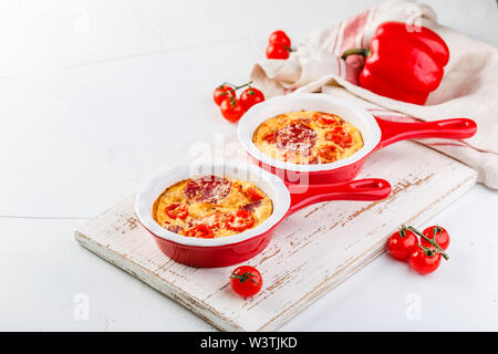 Frittata aux poivrons doux frais, tomates et de salami. Omelette italienne en céramique rouge poêlons sur un fond blanc. Close up Banque D'Images