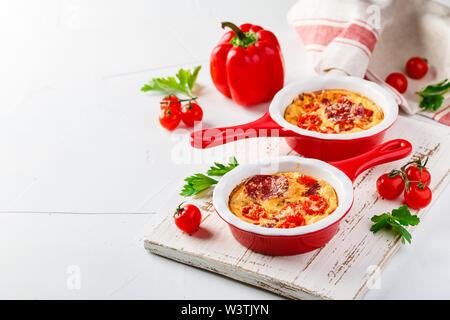 Frittata aux poivrons doux frais, tomates et de salami. Omelette italienne en céramique rouge poêlons sur un fond blanc. Close up Banque D'Images